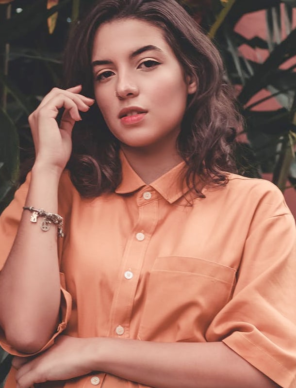 Brunette woman in a peach blouse posing against a floral backdrop.