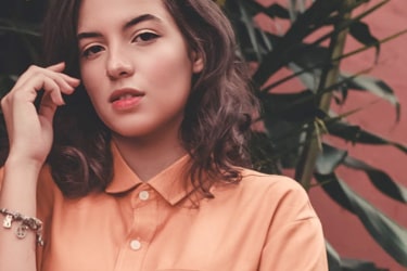 Brunette woman in a peach blouse posing against a floral backdrop.